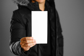 A man in a warm winter jacket holding a white leaflet. Blank paper. Close up. Isolated background