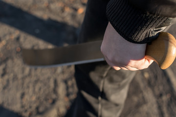 machete in the hand of a man on the street in black clothes - obrazy, fototapety, plakaty