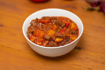 Meat stew with beef, potato, carrot, onion, spices,tomato and pepper . Slow cooked meat stew, bowl, wooden background. Hot autumn-winter dish. Close up.