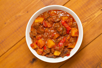 Meat stew with beef, potato, carrot, onion, spices,tomato and pepper . Slow cooked meat stew, bowl, wooden background. Hot autumn-winter dish. Close up.