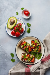 Avocados, cherry tomatoes and feta cheese sandwiches with balsamic sauce and cilantro on old olive board. Top view.
