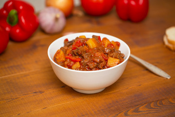 Meat stew with beef, potato, carrot, onion, spices,tomato and pepper . Slow cooked meat stew, bowl, wooden background. Hot autumn-winter dish. Close up.