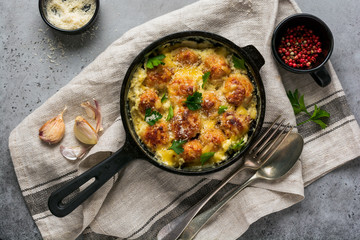 Meatballs with cheese and cream sauce in cast iron pan on gray vintage background. Top view.