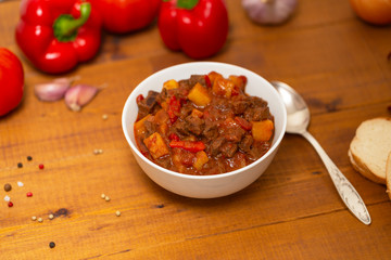 Meat stew with beef, potato, carrot, onion, spices,tomato and pepper . Slow cooked meat stew, bowl, wooden background. Hot autumn-winter dish. Close up.