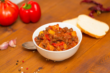 Meat stew with beef, potato, carrot, onion, spices,tomato and pepper . Slow cooked meat stew, bowl, wooden background. Hot autumn-winter dish. Close up.