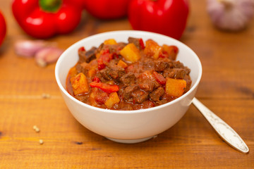 Meat stew with beef, potato, carrot, onion, spices,tomato and pepper . Slow cooked meat stew, bowl, wooden background. Hot autumn-winter dish. Close up.