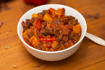 Meat stew with beef, potato, carrot, onion, spices,tomato and pepper . Slow cooked meat stew, bowl, wooden background. Hot autumn-winter dish. Close up.