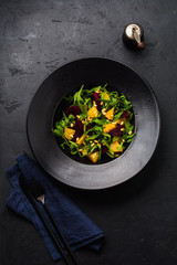 Beets, orange, pine nut, olive oil, feta cheese and arugula salad in black ceramic plate on dark concrete table background. Top view.