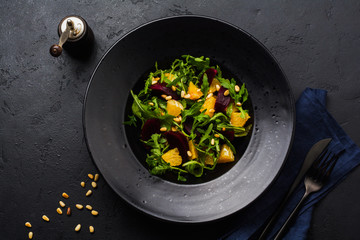 Beets, orange, pine nut, olive oil, feta cheese and arugula salad in black ceramic plate on dark concrete table background. Top view.