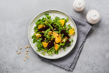 Beets, orange, pine nut, olive oil, feta cheese and arugula salad in ceramic plate on old concrete...