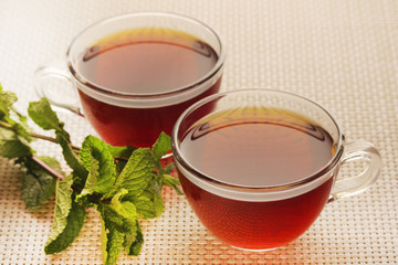 Two cups with black tea with fresh leaves of mint	