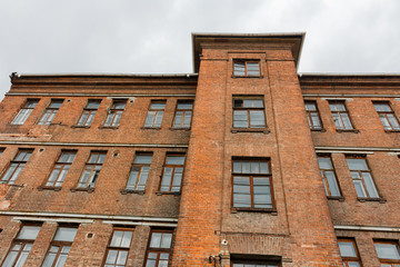 Obraz premium Upward view to old red brick wall building with windows and cloudy sky on the background