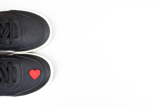 Black sneakers with little red heart on one of it on white background with copy space for text.