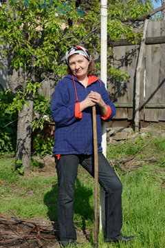 Woman is standing with rake near pole and pear tree.
