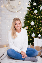 happy young woman sitting in living room with decorated Christmas tree