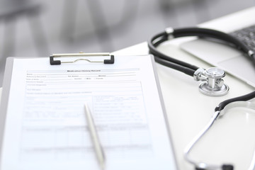 Stethoscope, clipboard with medical form lying on hospital reception desk with laptop computer. Medical tools at doctor working table.Medicine aтв health care concept