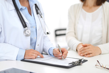 Unknown doctor and  female patient  discussing something while standing near reception desk in emergency hospital. Physician at work in clinic. Medicine and health care concept