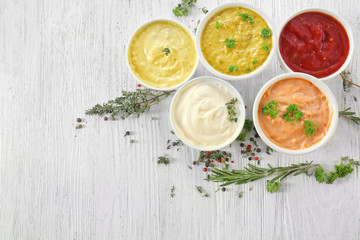 Different tasty sauces in bowls with spices on white wooden table