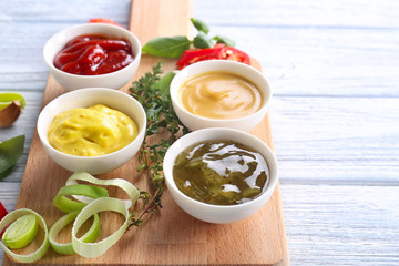 Different tasty sauces in bowls on wooden board