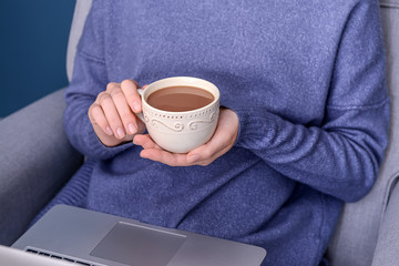 Woman drinking aromatic coffee while using laptop, closeup