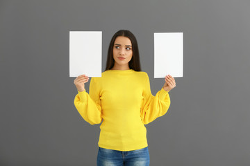 Emotional young woman with blank sheets of paper on grey background
