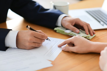 Businessman with bribe signing contract at table, closeup. Corruption concept