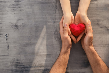 Loving young couple holding fabric heart on grey background