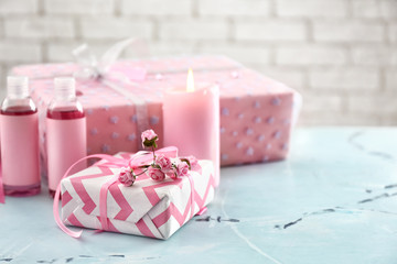 Beautiful gift boxes with cosmetics and burning candle on light table