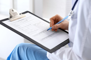 Woman doctor at work at hospital. Young female physician write prescription or filling up medical form while sitting in hospital office, close-up