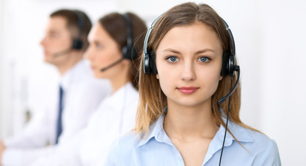 Call center operators. Focus on young cheerful smiling woman in headset. Business and customer service concepts