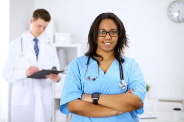 Female african american medical doctor with colleagues in background at hospital. Medicine and health care concept