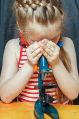 A little girl is studying a microscope.