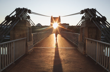 Person walking on the monumental Passerelle du College footbridge in Lyon during sunrise.