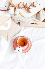 Cup of hot tea branch of cotton wooden tray knitted plaid sweater open notebook love letter in bed. Cozy morning breakfast at home. Lifestyle gentle background Copy Space autumn winter concept