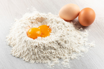 pile of flour with egg yolks for dough on table