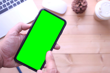 business man holding green screen smartphone and point on office table desk background