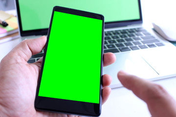business man holding green screen smartphone with point on office desk table background