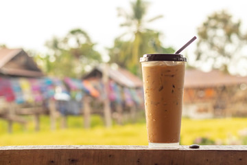 Iced coffee on the wooden floor behind a paddy field and colorful fabrics.