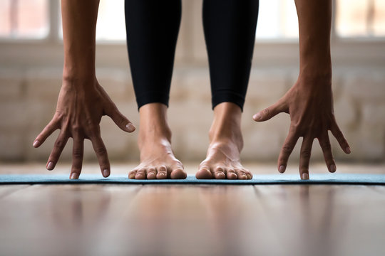 Sporty active woman practicing yoga, doing Standing forward bend exercise, head to knees uttanasana pose, wearing black sportswear pants, indoor close up, yoga studio or home. Well being concept
