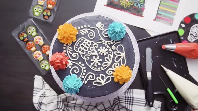 Time lapse. Step by step. Flat lay. Baker piping colorful buttercream italian icing on a top of multilayer cake for Dia de los Muertos holiday.
