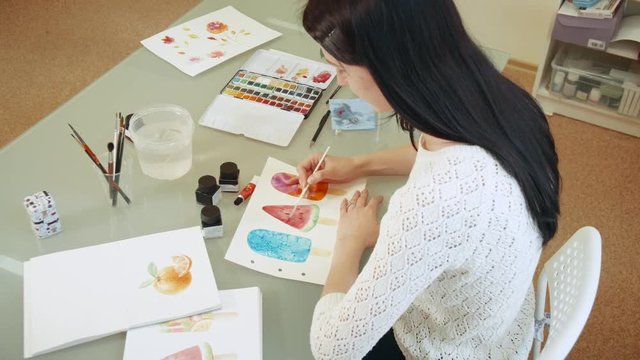 Young woman artist draw picture with watercolor paints and glanced at the camera.