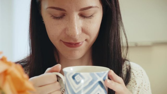 Portrait of young attractive girl sipping tea from cup sitting at the workplace. Close-up.