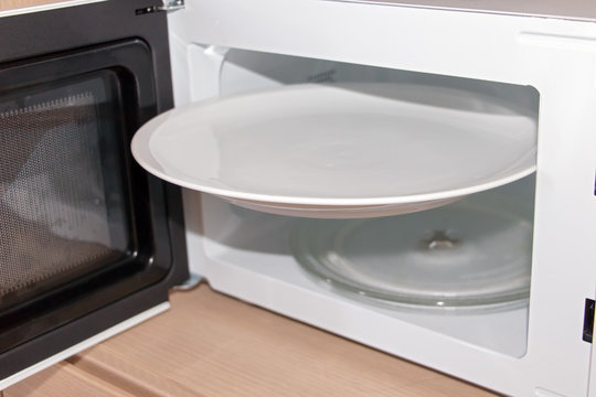 an open microwave with a white plate. An empty large disc is wedged in a microwave oven.