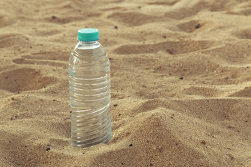 Bottle with crystal clear drinking water with a red lid on the sand on a hot, sunny day closeup.