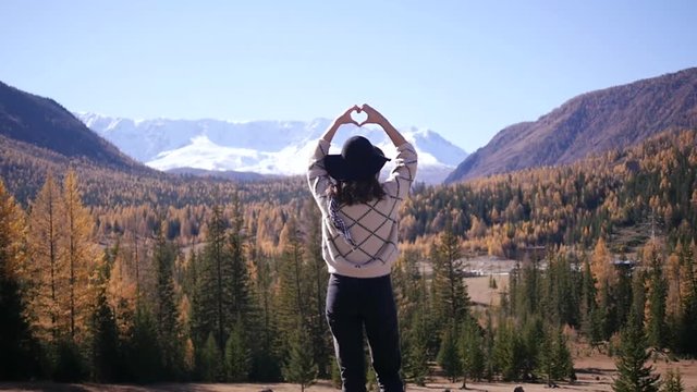 A woman with raised hands on top of a mountain looking at the view. The girl raises her hand up, noting the scenic landscape, enjoying nature, traveling adventure. Gorny Altai on the way to Mangolia