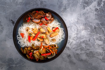 Traditional Asian food - rice noodles with seafood, salad, red pepper and fried mushrooms are on the side table. Copy space. Top view