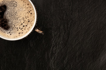 A closeup photo of black coffee in a vintage cup, shot from the top on a black slate background with a place for text