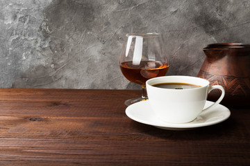 Coffee in white cup with cognac and clay cezve on wooden background. Copy space. Food background