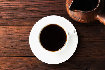 Coffee in white cup and clay cezve on wooden background. Top view. Food background