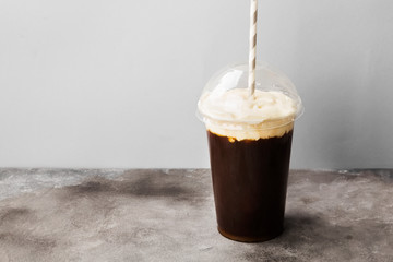 Coffee in plastic takeaway cup with cream on gray background. Copy space. Food background